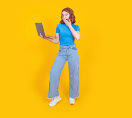 Shocked emotional woman, full body view photo of 20s caucasian shocked emotional woman. Using laptop, smiling looking screen closing open mouth with hand. Isolated yellow background, copy space.