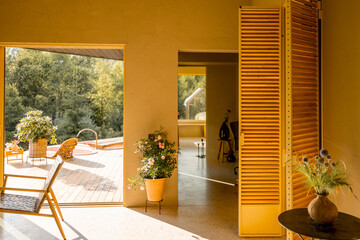 A cozy living space with bright yellow shutters leads to a spacious garden terrace. The warm, natural light fills the room, highlighting a vase of wildflowers and wooden furniture