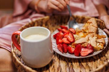 A woman is having breakfast in bed. tray with apple pie and fresh strawberries. morning coffee.