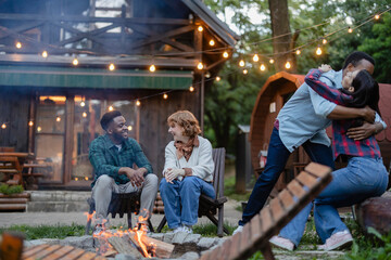 Friends gathering around bonfire, celebrating outside wooden cabin