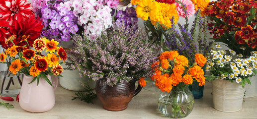 bouquets in vases and jugs stand in a row on the table, different flowers on the shop window. floral background.