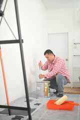 Young asian man wearing plaid shirt painting white wall in newly renovated room