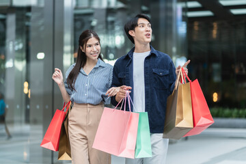 Beautiful Asian couple enjoy shopping together,young couple holding shopping bags,red bag,gold bad,Couple looking on the shopwindow while standing with shopping bags near the mall,christmas shopping