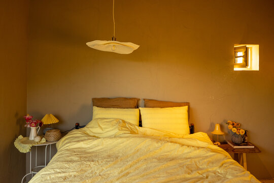 Softly lit bedroom with a warm yellow palette, highlighting a cozy bed and minimalist decor. A small window casts natural light, adding to the tranquil and inviting ambiance