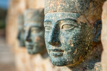 Fototapeta premium Ancient Egyptian stone statues with weathered patina. Archaeological artifacts showing traditional sculptural heads. Historical art exhibition display with blur effect and copy space