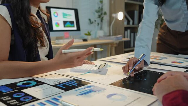 Team of business people or financial analysts working together, discussing using tablets and laptops and graphing data, planning, explaining, presenting project analysis results in modern office.