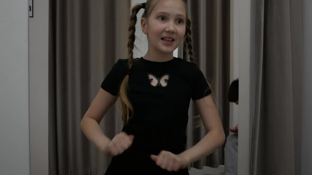 Playful, cheerful, attractive girl dancing in front of the mirror in the store fitting room. Teenager, getting ready for a walk, blog, movements, clothes, fashion, beauty and style.