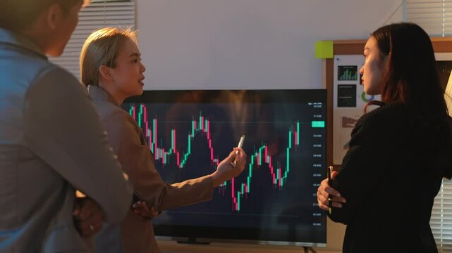 Investors brainstorming, planning, pointing at digital TV screen showing stock market index to analyze stock charts, investing, making profit, trading stock market and currency data in office.