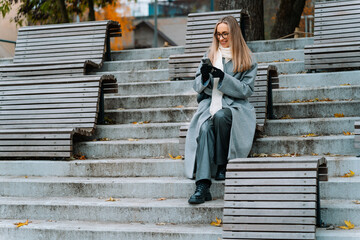 Smiling woman in glasses sitting on steps with a smartphone