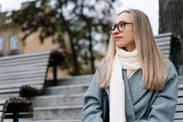 woman in grey coat and white scarf sitting on a bench outdoors
