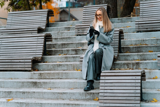 Smiling woman in glasses sitting on steps with a smartphone