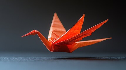 An intricately folded orange origami crane appears to be in mid-flight against a dark background.