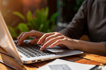 A close-up of a woman typing on a laptop keyboard, working remotely, sitting at an outdoor table.