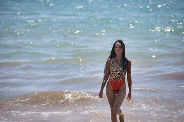 Young, beautiful, brunette woman, wearing a leopard swimsuit, posing happy and contented on the shore of the beach with the sea in the background. Concept beauty, fashion, trendy, femininity.