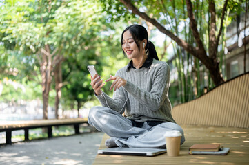 A woman sits on a park bench, selecting music on her phone, enjoys listening through her earphones.