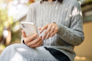 A woman in cozy clothes sitting on a park bench, enjoys listening to music through her earphones.