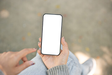 A close-up of a woman sitting outdoors in a park, using her smartphone, touching the screen.