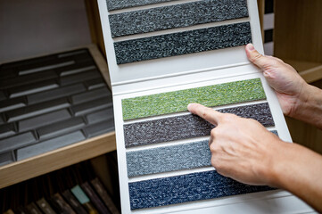 Designer hand pointing at sample fabric pieces on carpet swatch collection. Customer choosing color...