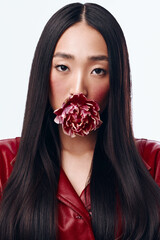 Sensual Asian woman with long black hair holding a delicate flower in front of her mouth