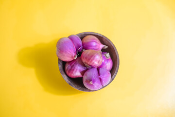 red onion in wooden bowl on yellow background 