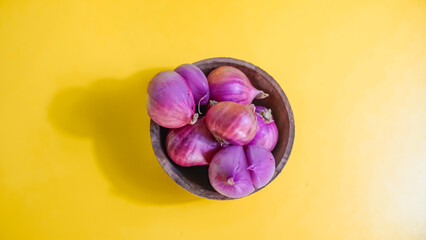 red onion in wooden bowl on yellow background 
