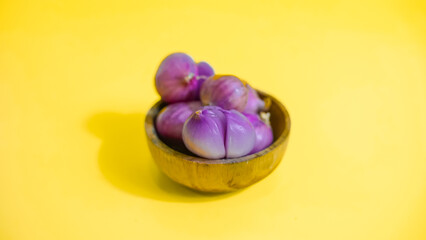 red onion in wooden bowl on yellow background 