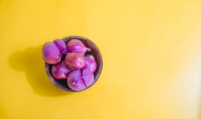 red onion in wooden bowl on yellow background 