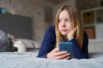  Unhappy Teenage Girl With Mobile Phone Lying On Bed At Home Anxious About Social Media Online Bullying And Using Phone Too Much