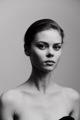 Elegant young woman with minimal makeup and a neutral expression, showcasing beauty and simplicity against a soft grey background. Portrait and fashion concept.