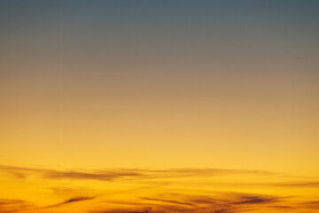 Thin wispy clouds swirl at the bottom of a vivid orange sunset sky in transition to the dark hues of night, creating a tranquil image suitable for use as a wallpaper background.