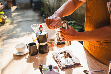 Barista is grinding coffee beans with manual stainless steel grinder to make black coffee machine, brewing equipment or coffee drip set Dripper on a wooden table In the kitchen at home in the morning