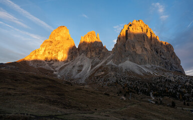 Golden sunrise light on the Sassolungo Dolomite mountains above an alpine meadow and trail