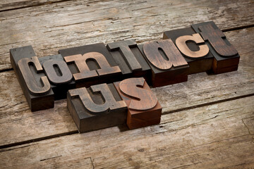 contact us, phrase written with vintage letterpress printing blocks, angled view, rustic wooden...