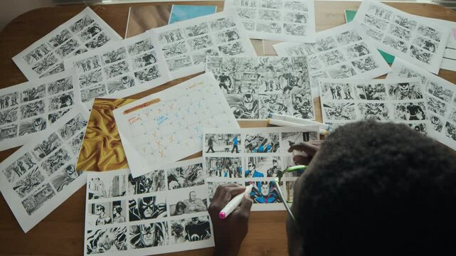 Top view shot of African American male storyboard artist using colored markers while creating sheets at wooden table in creative workspace