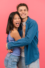 A joyful young couple in casual clothing, hugging and smiling at the camera. They share a fun moment together against a vibrant pink background. Perfect for love, relationship, and happiness themes.