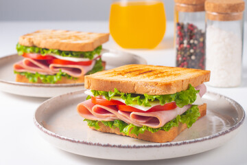 Close-up of two sandwiches with bacon, salami, prosciutto and fresh vegetables on rustic wooden cutting board. Club sandwich concept