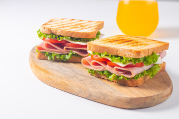 Close-up of two sandwiches with bacon, salami, prosciutto and fresh vegetables on rustic wooden cutting board. Club sandwich concept