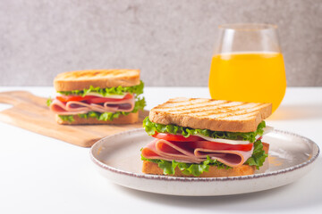 Close-up of two sandwiches with bacon, salami, prosciutto and fresh vegetables on rustic wooden cutting board. Club sandwich concept