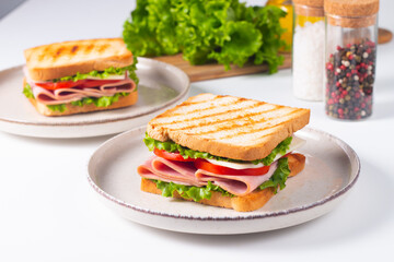 Close-up of two sandwiches with bacon, salami, prosciutto and fresh vegetables on rustic wooden cutting board. Club sandwich concept