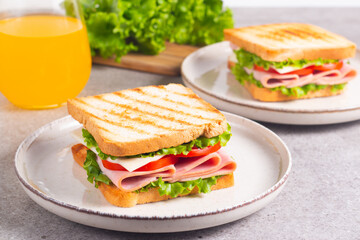 Close-up of two sandwiches with bacon, salami, prosciutto and fresh vegetables on rustic wooden cutting board. Club sandwich concept