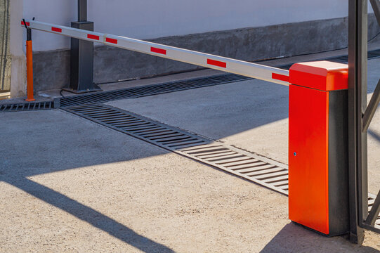 A bright orange barrier with a white overlap and red reflective stripes stands at the entrance, regulating access to movement on this driveway