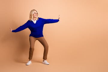 Elegant mature woman showing confidence in blue jumper against beige background, embracing leisure...