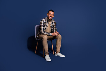 Fototapeta premium Full length photo of cheerful positive guy dressed plaid shirt sitting chair emtpy space isolated blue color background