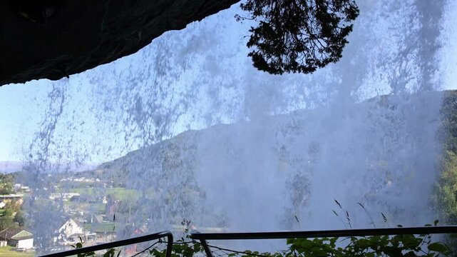 Handheld view beneath Steinsdalsfossen waterfall, showcasing the walkway and scenic Steinsdalen valley below