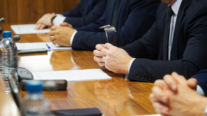 Man in suit holding prescription glasses while sitting next to colleagues during business meeting...