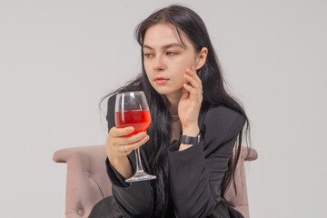 Cute young brunette girl with a wine glass sitting in a chair on a white background. Copy space