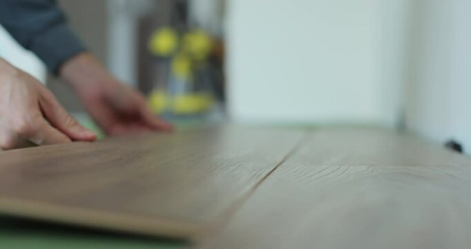 Man kneeling and installing wood laminate floor in a home. Closeup on male hands.