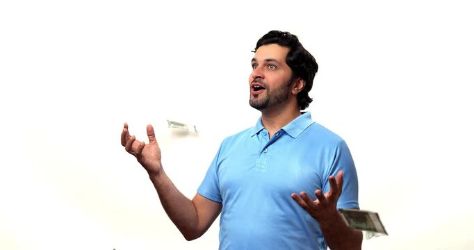 Happy Indian bearded young man catching and showing falling paper currency notes in a money rain, celebrating the joy of winning a lottery, savings, or receiving a bonus, isolated against a white