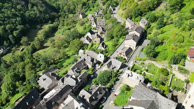 Drone aerial view in France countryside small old medieval town and a cathedral surrounded by a green mountain forest flying over in Conques