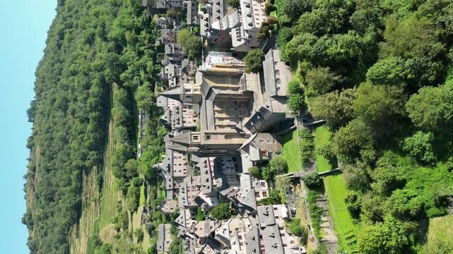 Drone aerial view in France countryside small old medieval town and a cathedral surrounded by a green mountain forest circling around in Conques portrait view